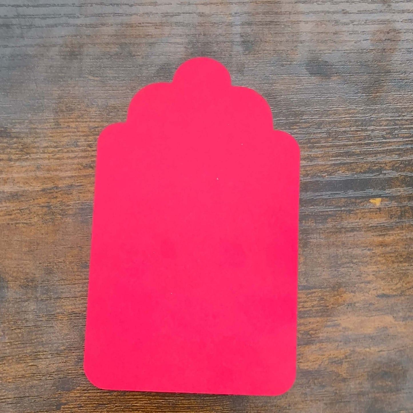 Back of a red scalloped gift tag, blank and ready for personal message, on rustic wooden surface