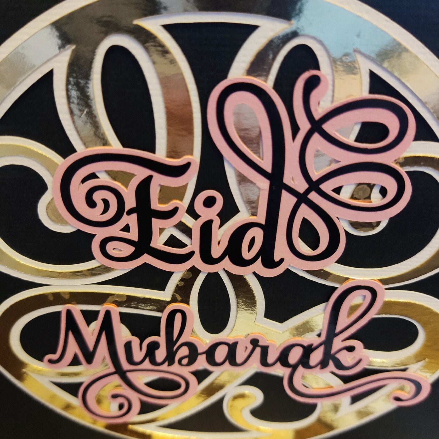 Detailed close-up of the Eid Mubarak lettering, showcasing the layered pink and black script and glossy gold foiled background.