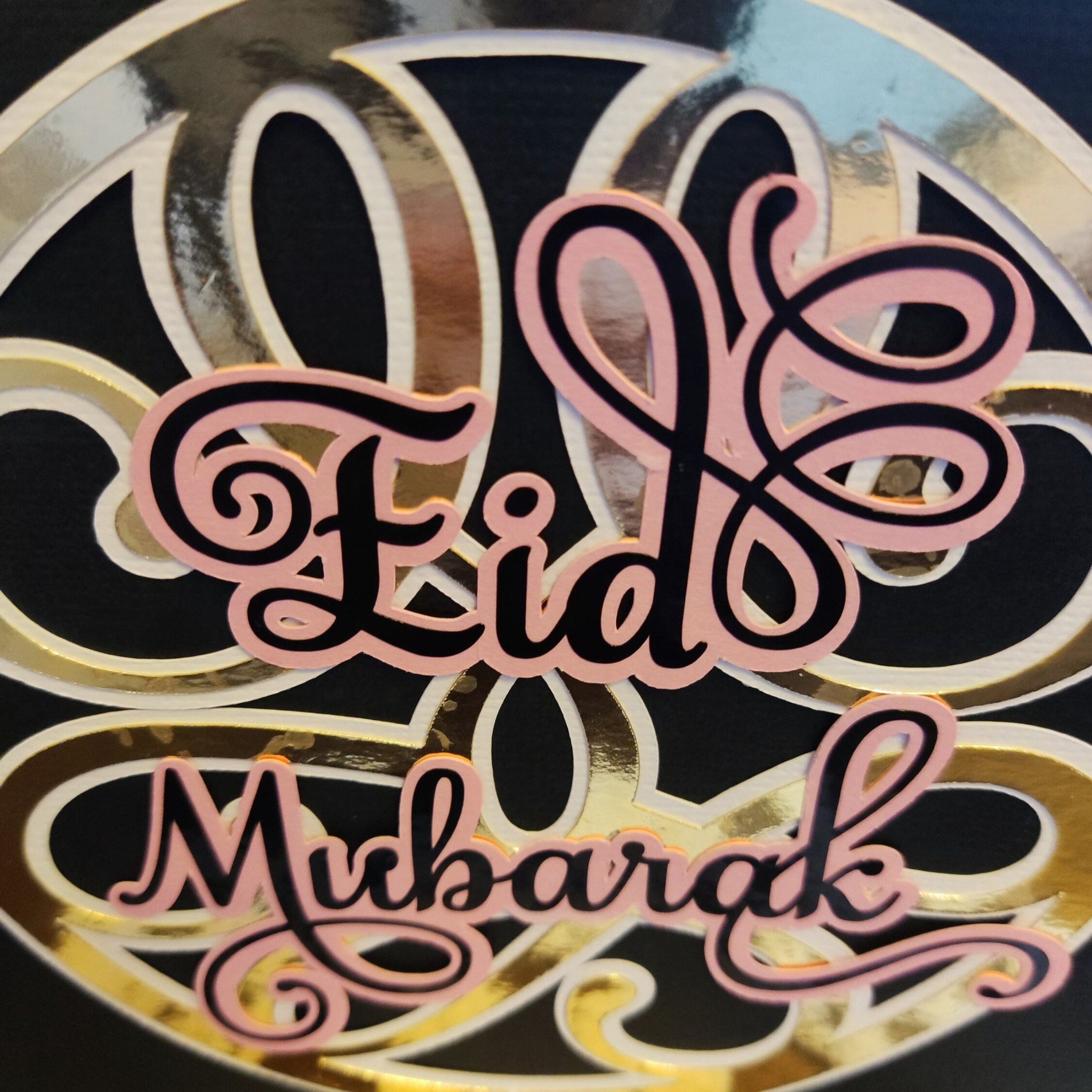 Detailed close-up of the Eid Mubarak lettering, showcasing the layered pink and black script and glossy gold foiled background.