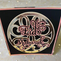 Elegant square Eid Mubarak card with a shiny gold circular design on a black background. Pink script lettering adds a soft, luxurious finish.