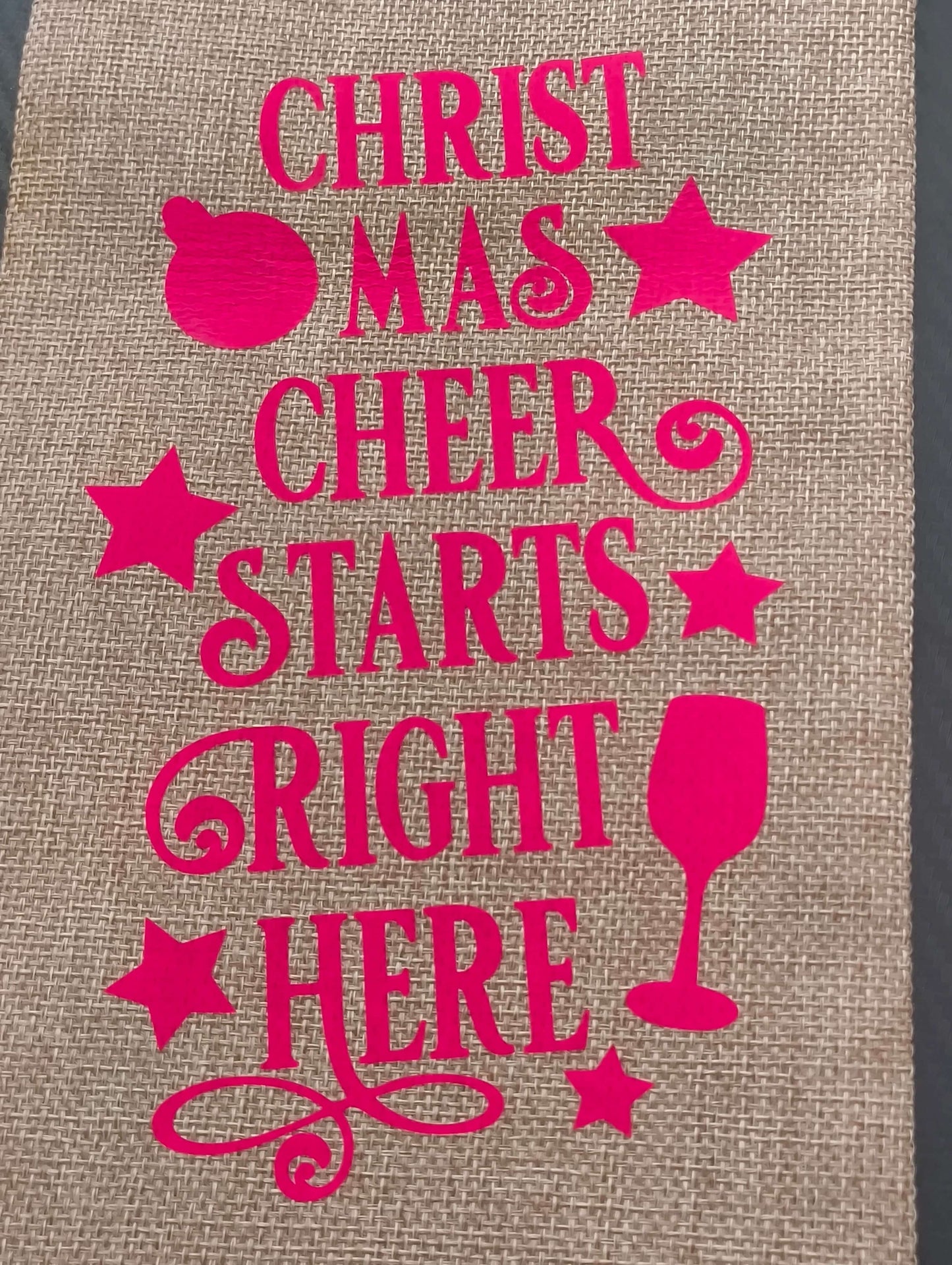 Funny Christmas wine bag with pink lettering saying 'Christmas Cheer Starts Right Here' on hessian fabric.