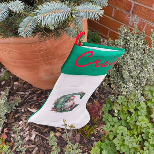 Personalised Vintage Santa Christmas Stocking hanging beside a flower pot with the name Craig embroidered on it.