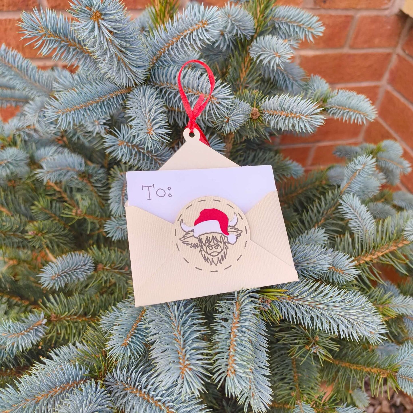 Festive handmade Christmas envelope ornament for gift cards hanging on pine tree with red ribbon