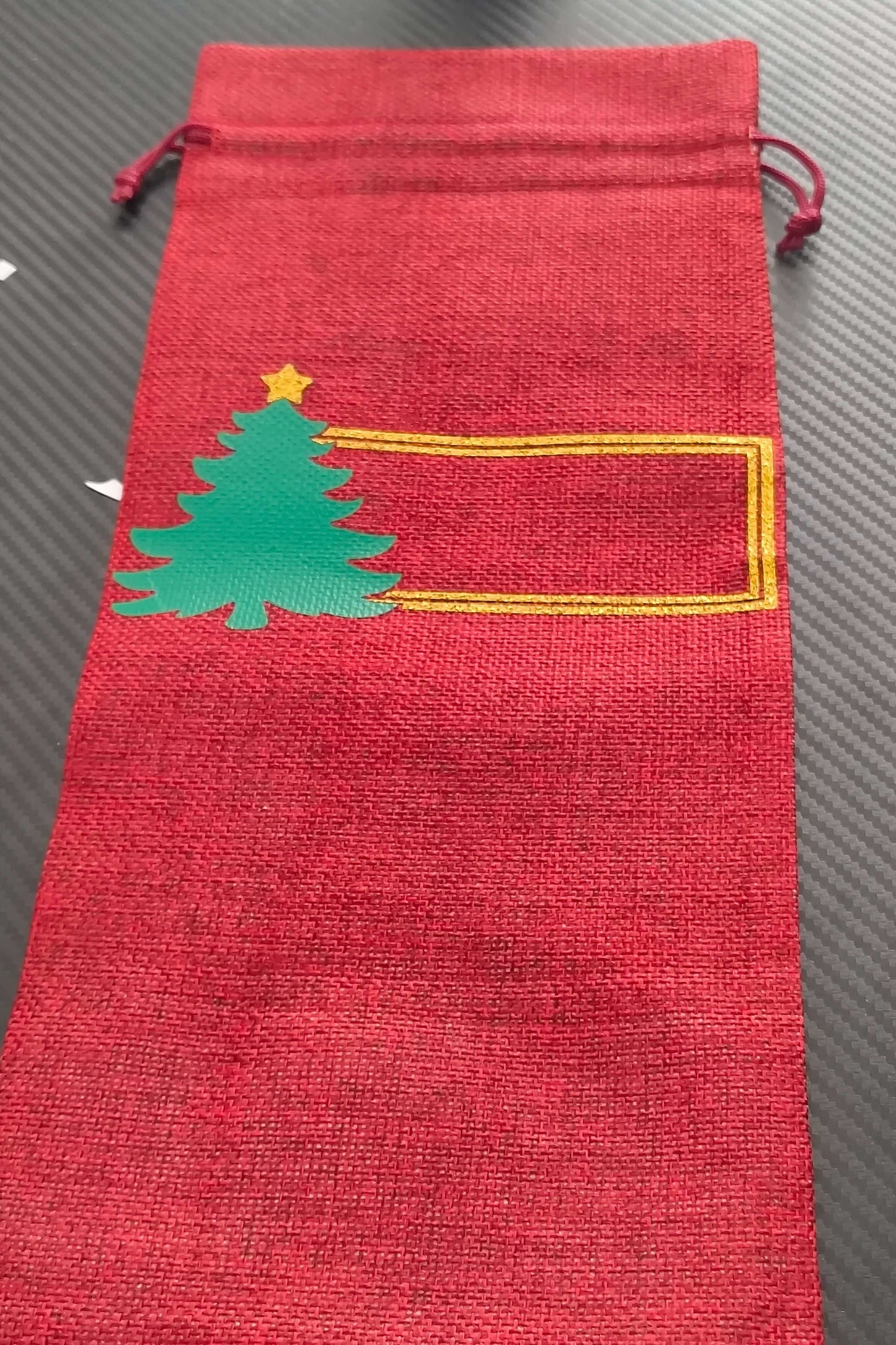 Personalised Christmas wine bottle bag in red hessian with green Christmas tree design and blank space for a name.