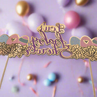 Mirrored gold and purple baby shower topper reading 'Lou's Baby Shower', surrounded by floral and baby-themed icons. The topper is set against a soft lavender background with pastel and gold balloons and ribbon decorations, creating a festive and dreamy atmosphere.