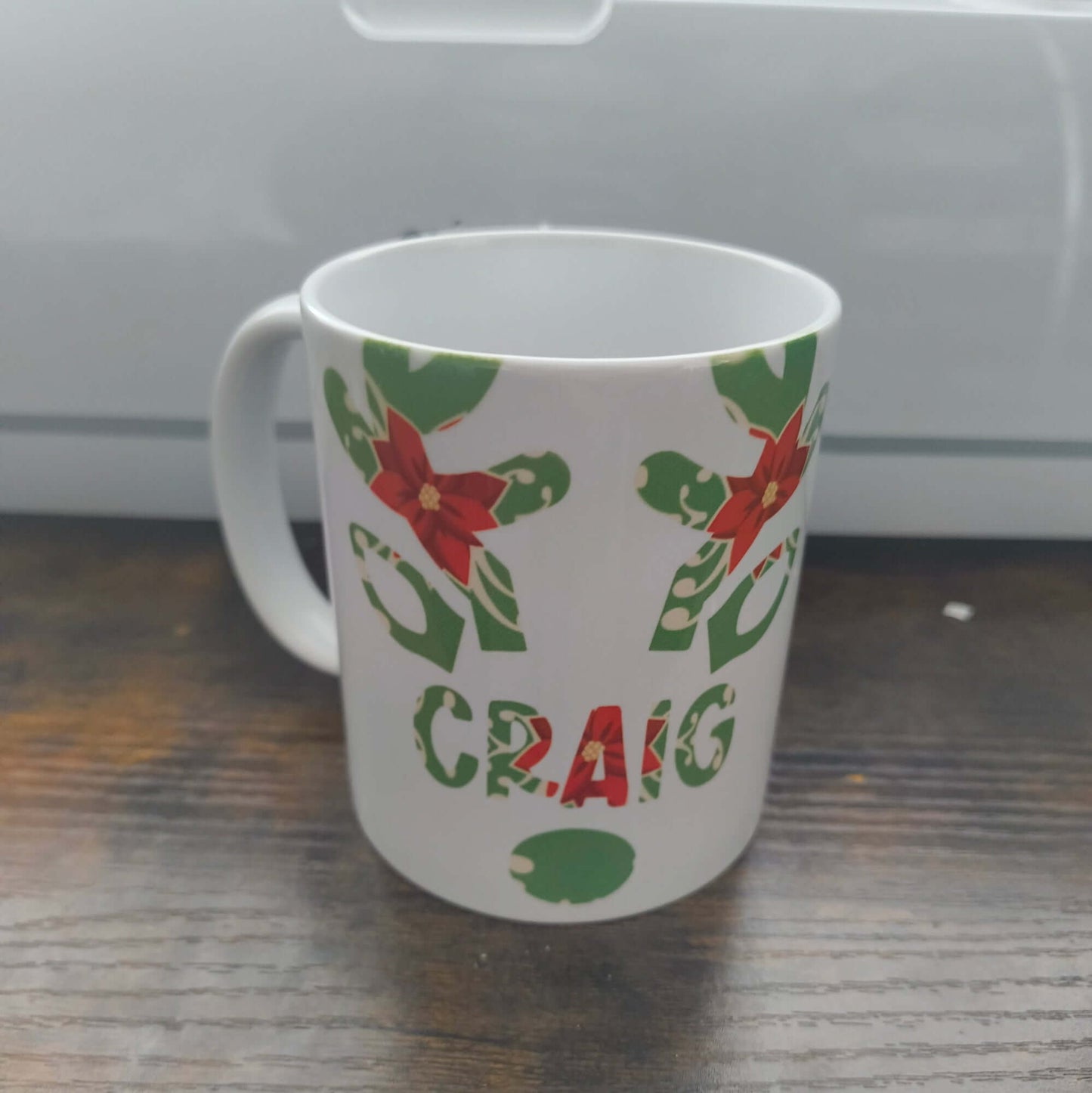 Personalised Christmas mug with poinsettia and holly design featuring the name Craig.