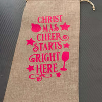 Festive hessian wine bag with pink text saying 'Christmas Cheer Starts Right Here' for eco-friendly gifting.