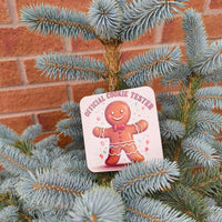 Fun gingerbread man “Official Cookie Tester” drinks coaster styled on an outdoor Christmas tree.