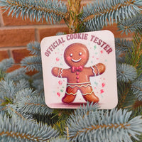 Square coaster with gingerbread man and “Official Cookie Tester” text displayed on a blue spruce tree.