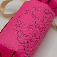 Personalised Birthday Crackers in bright pink with balloon design and golden ribbons for birthday celebrations.