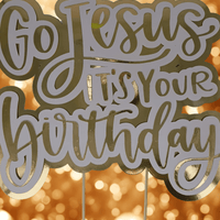 Gold and white “Go Jesus It’s Your Birthday” cake topper on a cake, with golden bokeh background for a festive celebration.