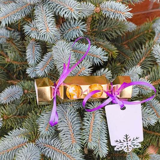 Personalised chocolate cracker gift hanging from a Christmas tree with a purple ribbon.