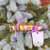 Personalised chocolate cracker gift hanging on a Christmas tree with purple ribbons and a tag.