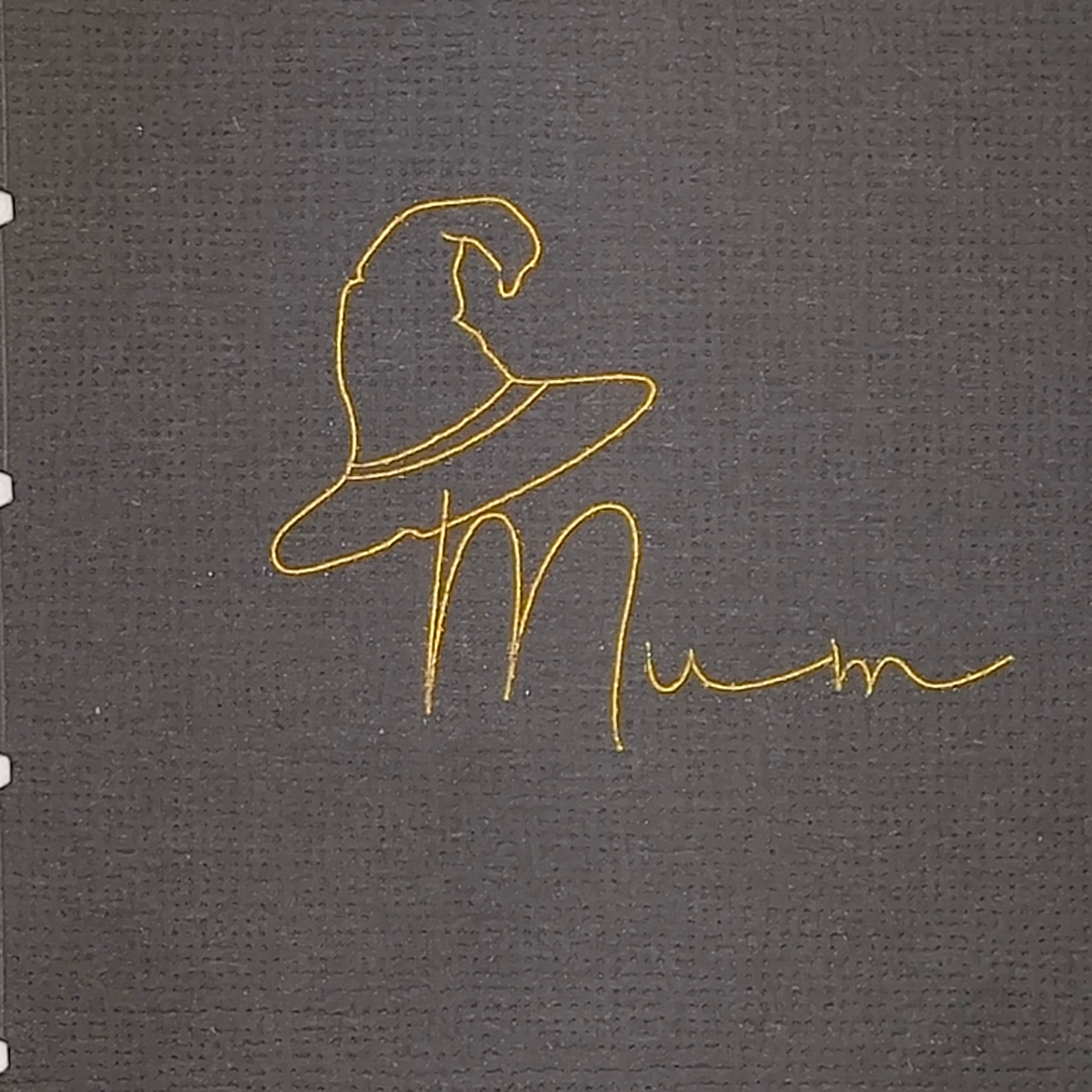 Detailed view of gold foil witch hat illustration and “Mum” text on textured black cracker cardstock
