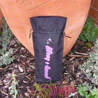 Full view of black drawstring wine gift bag with pink glitter “Groovy & Boozy” lettering, placed in front of terracotta pot.