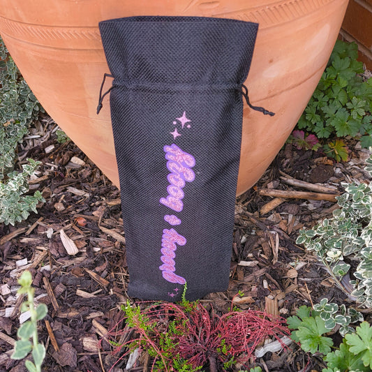 Black wine bag with sparkling pink “Groovy & Boozy” text shown upright outdoors among garden plants.