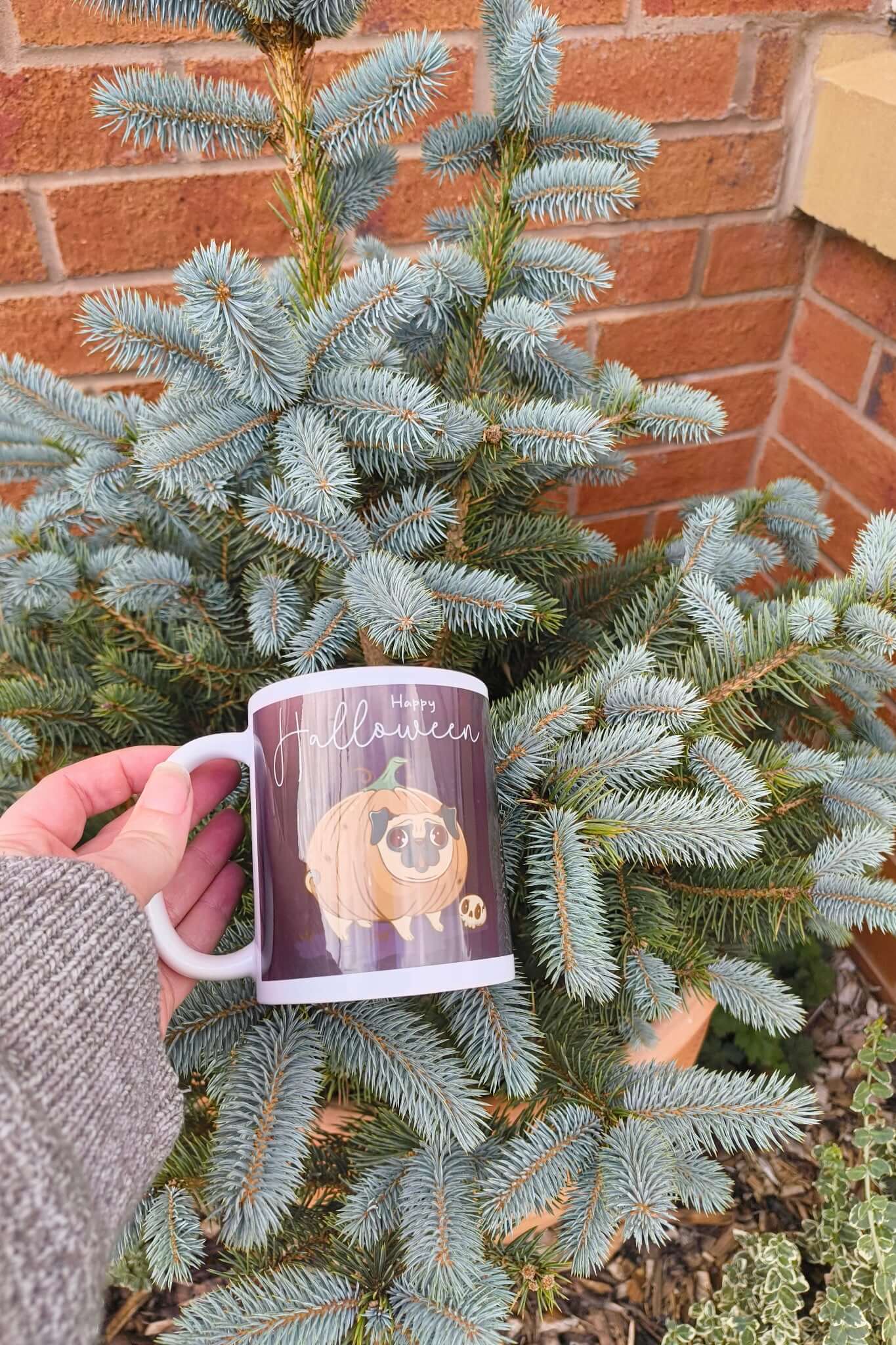 Close-up of Happy Halloween pug mug showing cute cartoon pug inside a pumpkin, with a small skull detail on a purple background.