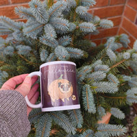 Person holding Happy Halloween mug with pug pumpkin design among fir tree branches, festive autumn outdoor photo.
