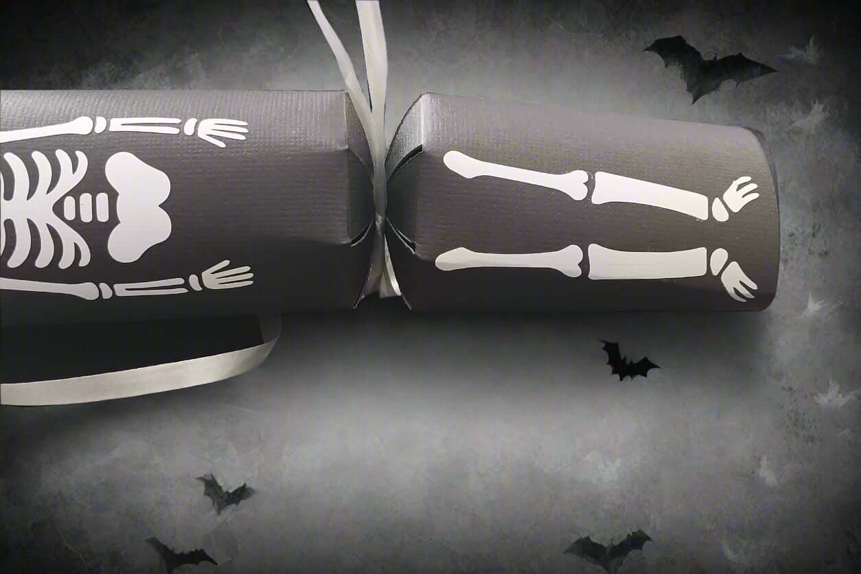 Halloween skeleton cracker with bones and ribcage design on black card, decorated with flying bat background.