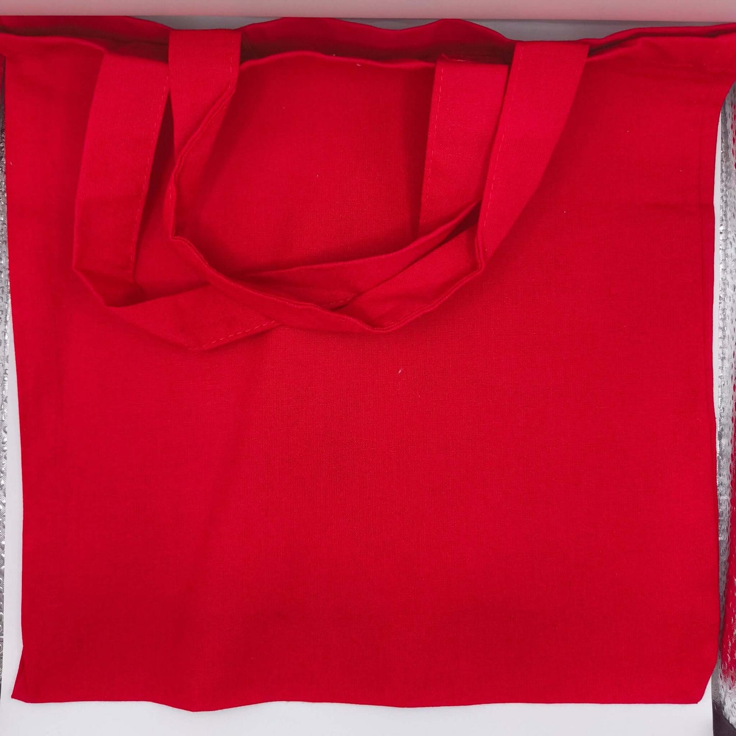 Plain back of red cotton tote bag, showing sturdy handles and quality stitching, reusable eco-friendly fabric.
