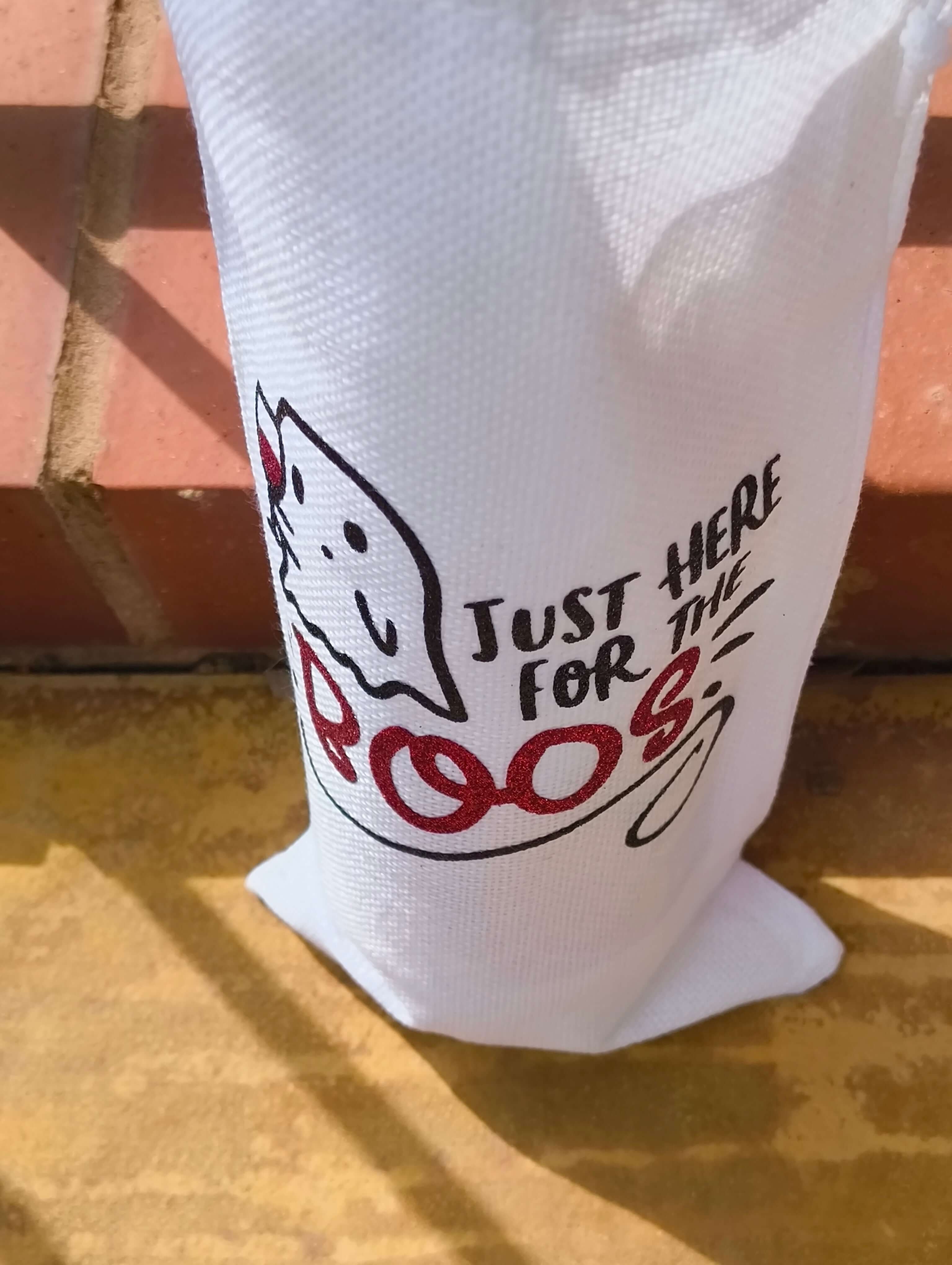 Close-up of Halloween wine bag with ghost and glitter red "BOOS" text, showing textured white fabric and bold design.