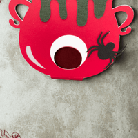 Colourful Halloween lollipop holder shaped like a cauldron, featuring a spider decoration and dripping green accents.