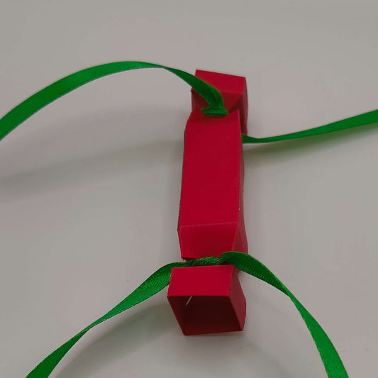 Side view of handmade red advent cracker with green ribbon ends