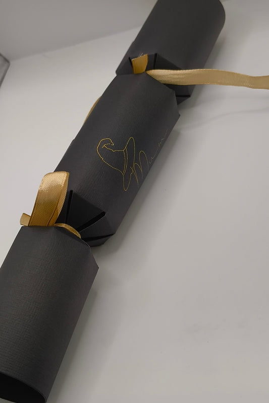 Handmade black cracker assembled with gold ribbon ties, featuring a witch hat “Mum” design in gold foil