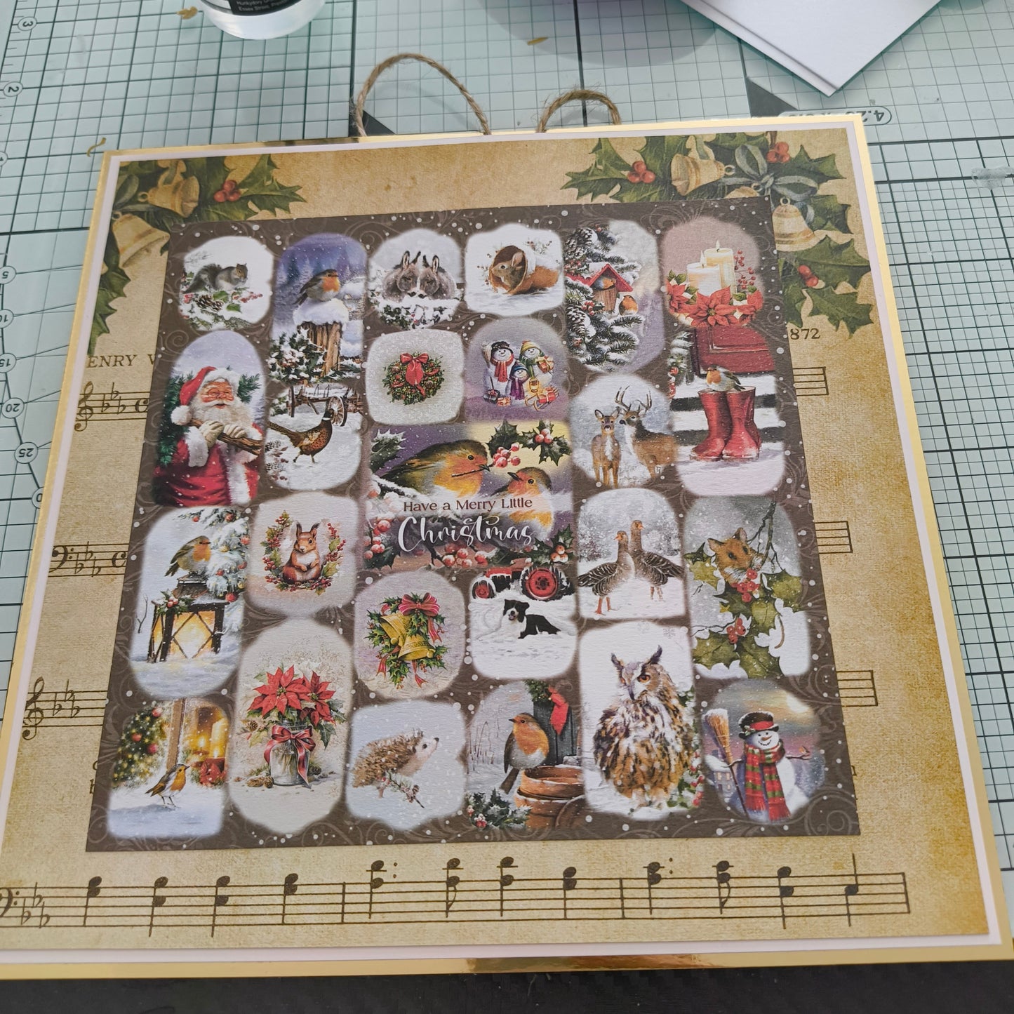 Handmade Christmas advent calendar decorated with vintage-style festive illustrations, including robins, owls, Santa Claus, wreaths, and winter animals, displayed on a craft mat with glue and scissors nearby.