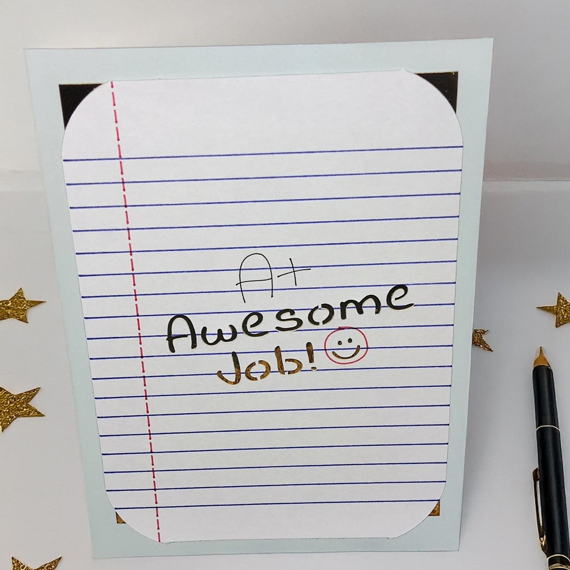 Handmade encouragement greeting card with A+ Awesome Job message, photographed from a top-down angle with gold star confetti and pen for school or student celebration keywords.