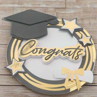 Handmade graduation card featuring a black mortarboard, gold “Congrats” text, gold stars, and diploma motif on a circular gold and white layered base. Ideal for graduation cards, scrapbook pages, and handmade gifts.