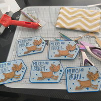 Set of handmade reindeer Christmas gift tags with “Merry and Bright” message, shown on crafting table with tools