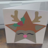 Handmade Christmas card featuring a reindeer with antlers, holly, and a pink nose on a star-shaped design.