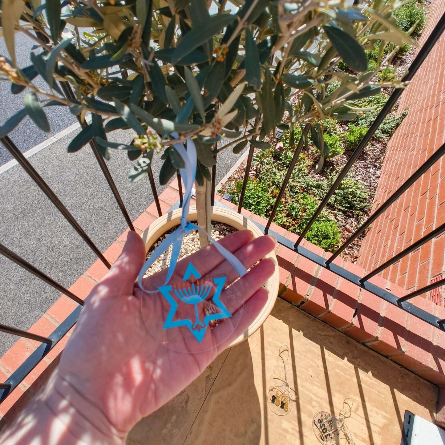 Person holding clear Hanukkah ornament with menorah and Star of David next to other acrylic decorations.