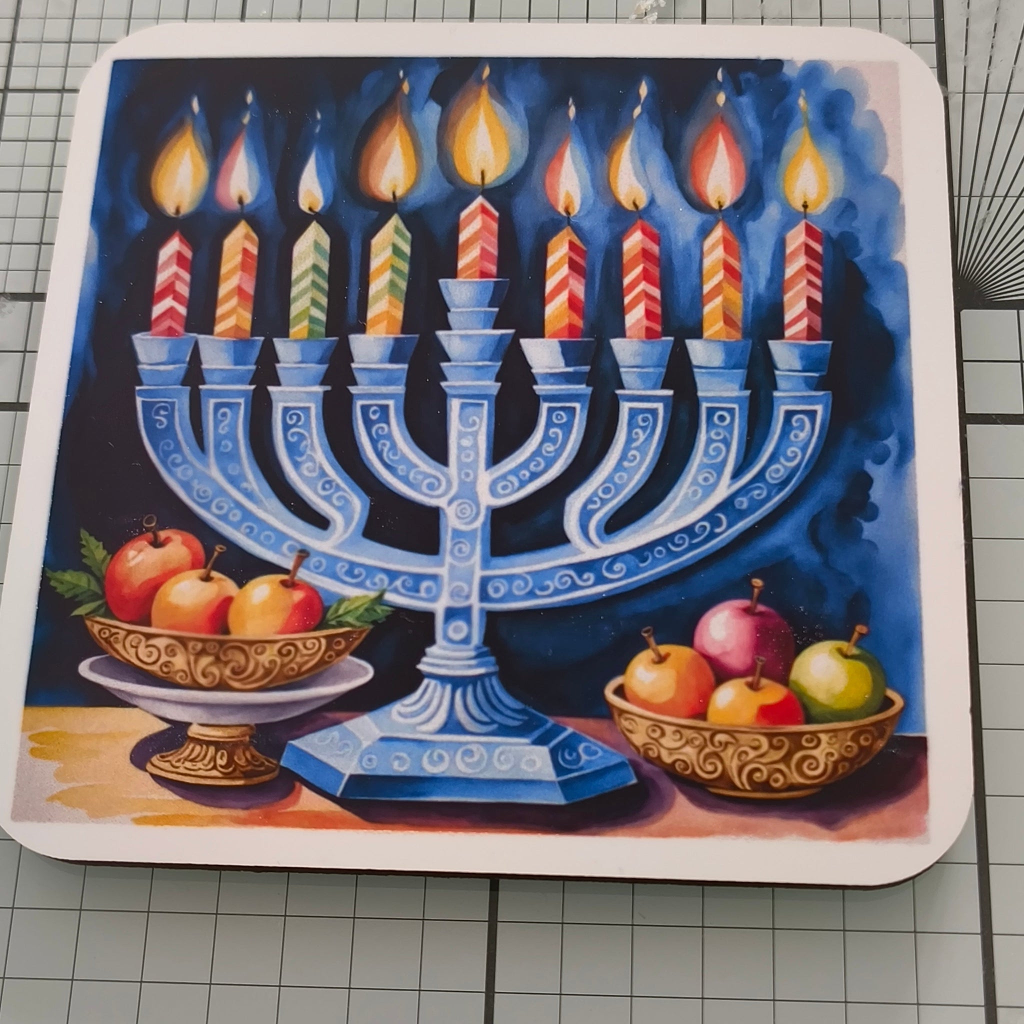 Close-up of Hanukkah coaster showing blue menorah with striped candles and festive fruit bowls