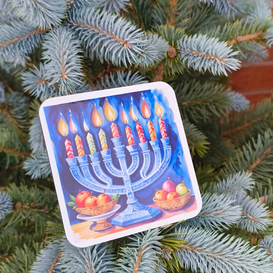 Festive Hanukkah coaster featuring a menorah design, placed among blue spruce tree branches