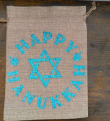 Flat lay of Hanukkah hessian gift bag with blue glitter Star of David and ‘Happy Hanukkah’ text