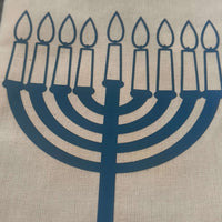 Close-up of a beige hessian gift bag with a blue vinyl Hanukkah menorah design, showcasing nine lit candles for the Jewish festival of lights.