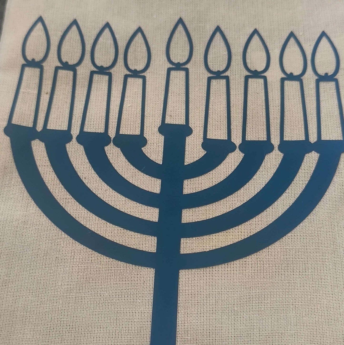 Close-up of a beige hessian gift bag with a blue vinyl Hanukkah menorah design, showcasing nine lit candles for the Jewish festival of lights.