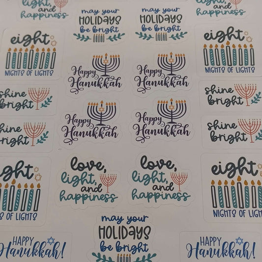 Top-down view of a Hanukkah sticker sheet featuring assorted festive designs including menorahs, candles, and phrases like “Shine Bright,” “Happy Hanukkah,” and “Eight Nights of Lights,” displayed on a white background.
