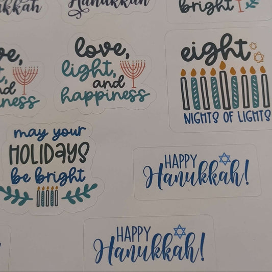 Close-up of Hanukkah sticker sheet featuring festive messages such as “Love, Light, and Happiness,” “Happy Hanukkah,” and “May Your Holidays Be Bright,” with menorahs, candles, and Stars of David on a white background.