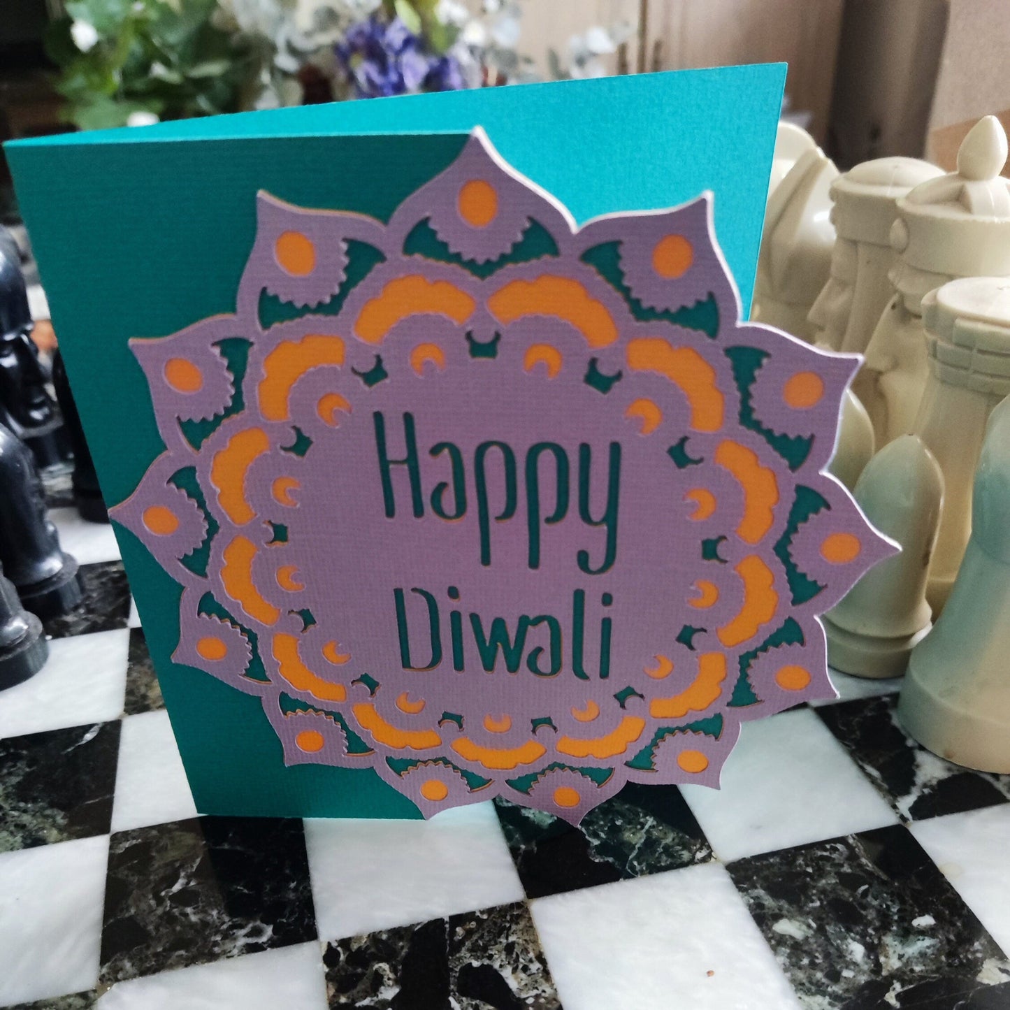 Square Diwali card with cut-out mandala and “Happy Diwali” text. Bright teal background with purple and gold layers adds depth and vibrancy.