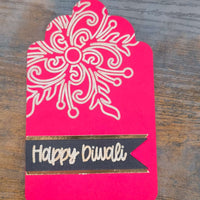 Red and gold Happy Diwali gift tag with intricate floral mandala pattern, viewed from above on wooden background