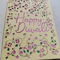 Close-up of a handmade Happy Diwali card featuring intricate floral cut-outs in pink and green against textured cream cardstock.