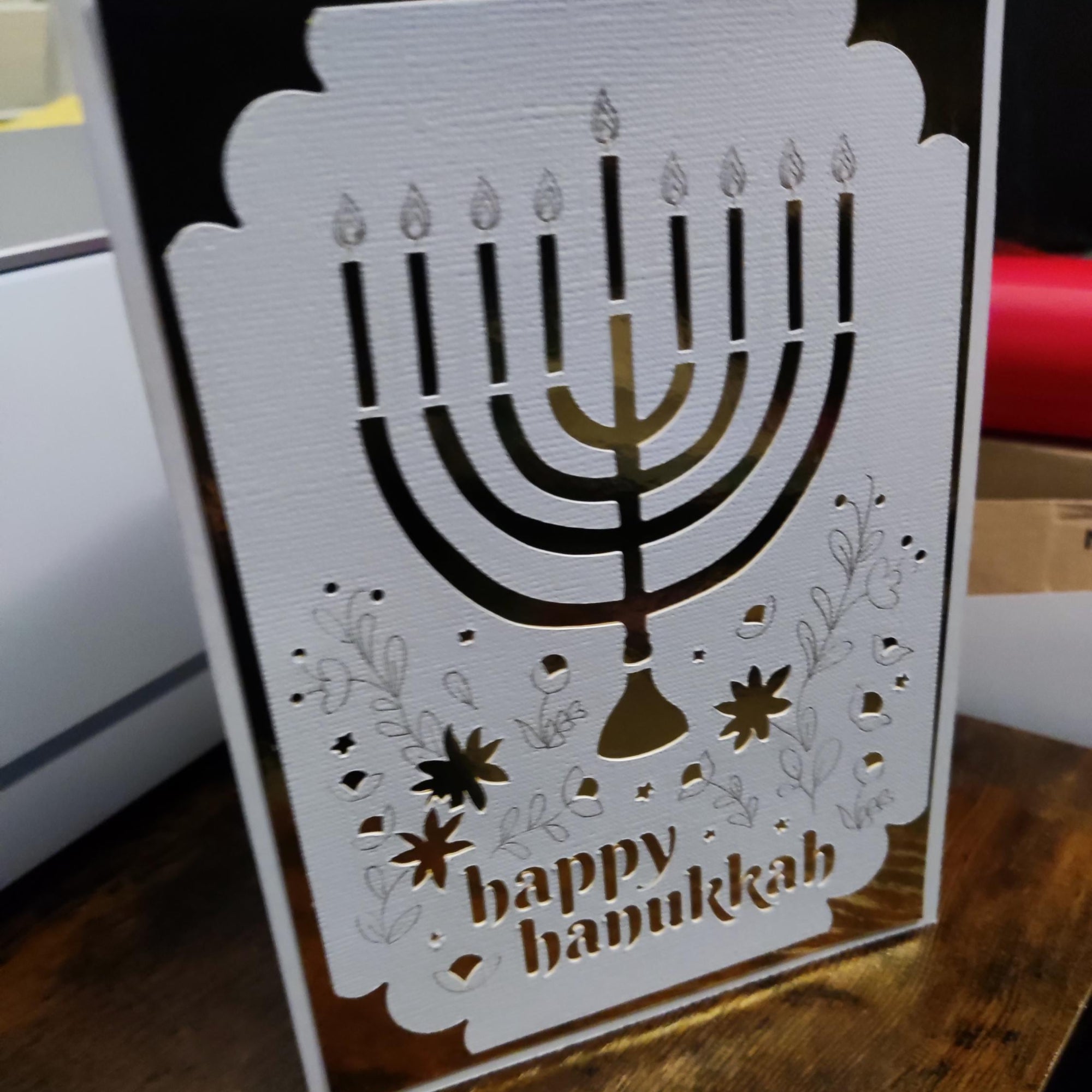 Festive Hanukkah greeting card with a gold foil menorah cut-out and delicate floral details, reading “Happy Hanukkah.”