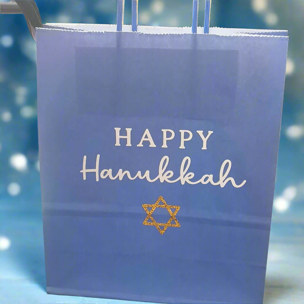 Blue Happy Hanukkah gift bag with white text and a gold glitter Star of David, displayed against a soft festive blue background with light bokeh effect.