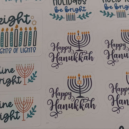 Close-up of Hanukkah sticker sheet featuring festive messages like “Happy Hanukkah,” “Shine Bright,” and “Holidays Be Bright,” with menorah and candle illustrations on a white background.

