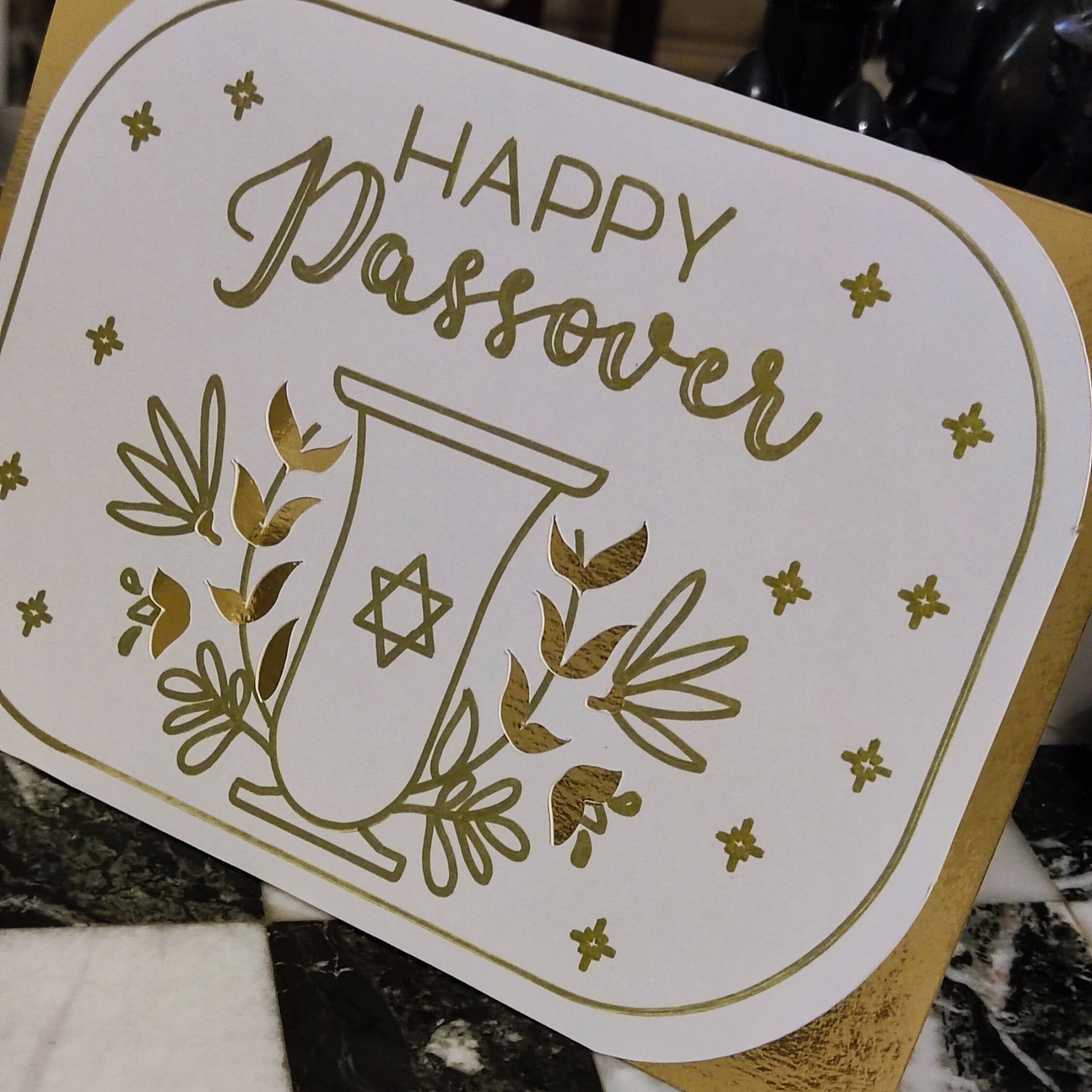 Angled view of the Passover card highlighting reflective gold foil details on the goblet and lettering. Shows shimmer and textured finish up close.