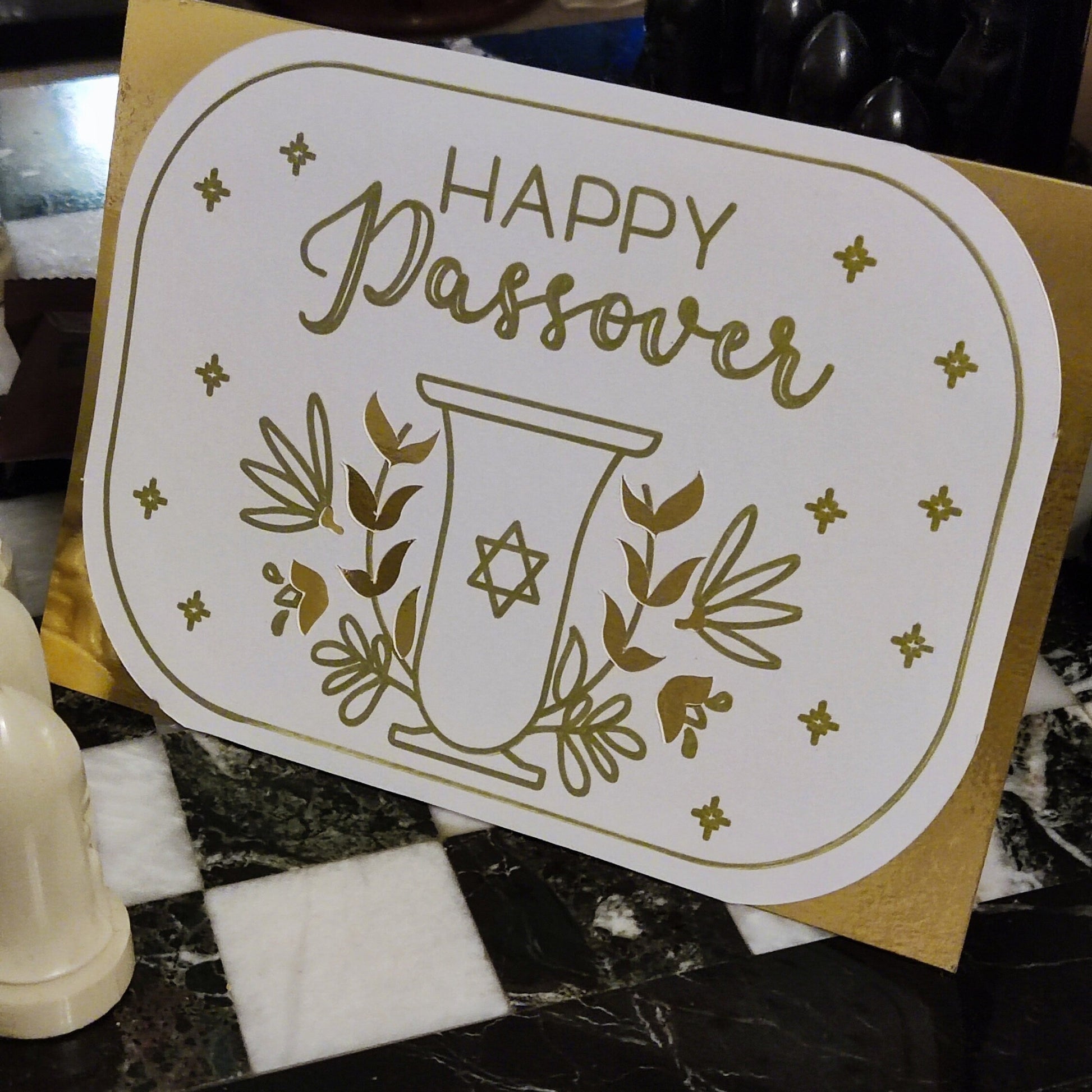 Elegant white card with gold foil “Happy Passover” design, featuring a Star of David goblet and floral motifs. Photographed upright to show full scale and shine.
