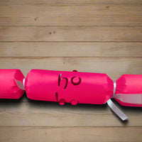 Close-up of red Christmas cracker with “Ho Ho” cut-out detail, tied with silver ribbon, placed on a wooden table for scale.